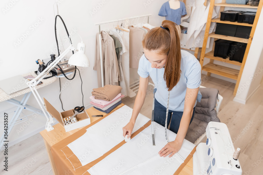 Obraz premium Top view Woman seamstress makes pattern with chalk on fabric for sewing clothes in tailor studio