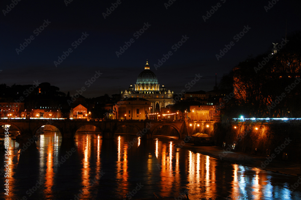 Night in Rome. View of the city along River Tiber with the iconic St Peter illuminated in a romantic atmosphere