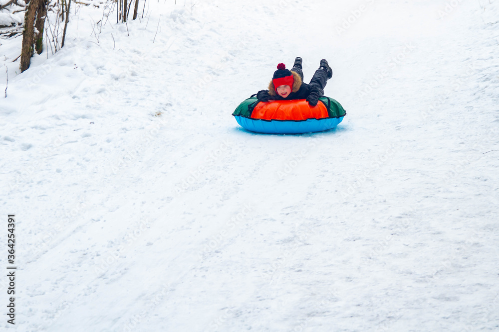 A boy rolls down a slide on snowtubes in the winter in the forest. Children's games in the snow. Snowy winter in Russia.