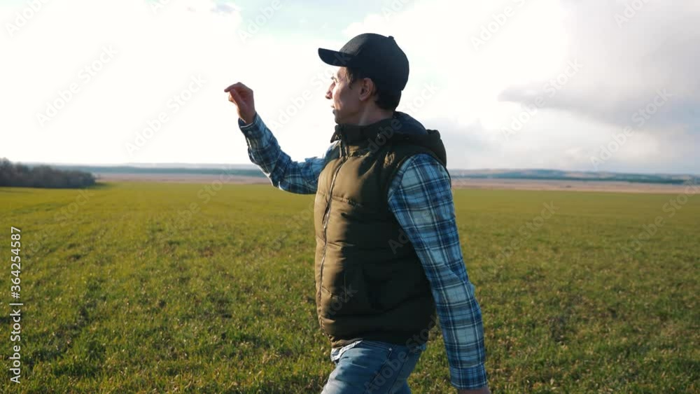 A male farmer walks on a green field, looking at his farm, the future harvest. A male farmer walks on a green field, looking at his farm, the future harvest.