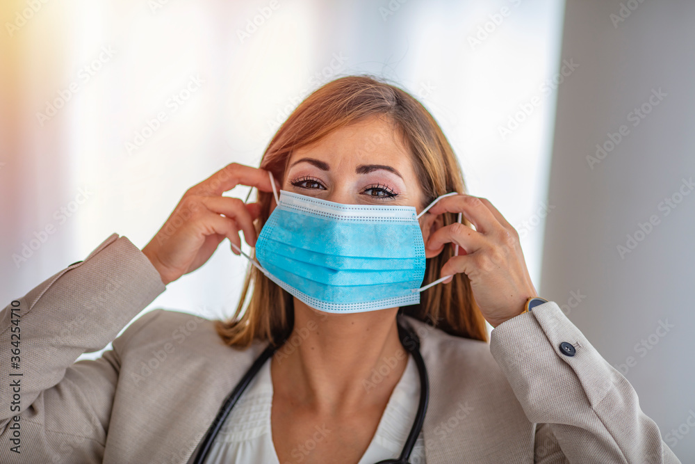 Young beautiful woman put on medical mask for protection against coronavirus contagious disease. on a light background. Medic holding face mask. Preventive measure against coronavirus COVID-19. Young beautiful woman put on medical mask for protection against coronavirus contagious disease. on a light background. Medic holding face mask. Preventive measure against coronavirus COVID-19.