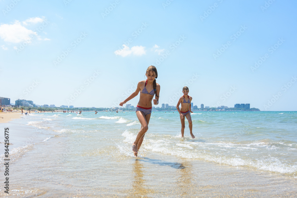 Two girlfriends run along the coastal strip of the sea coast