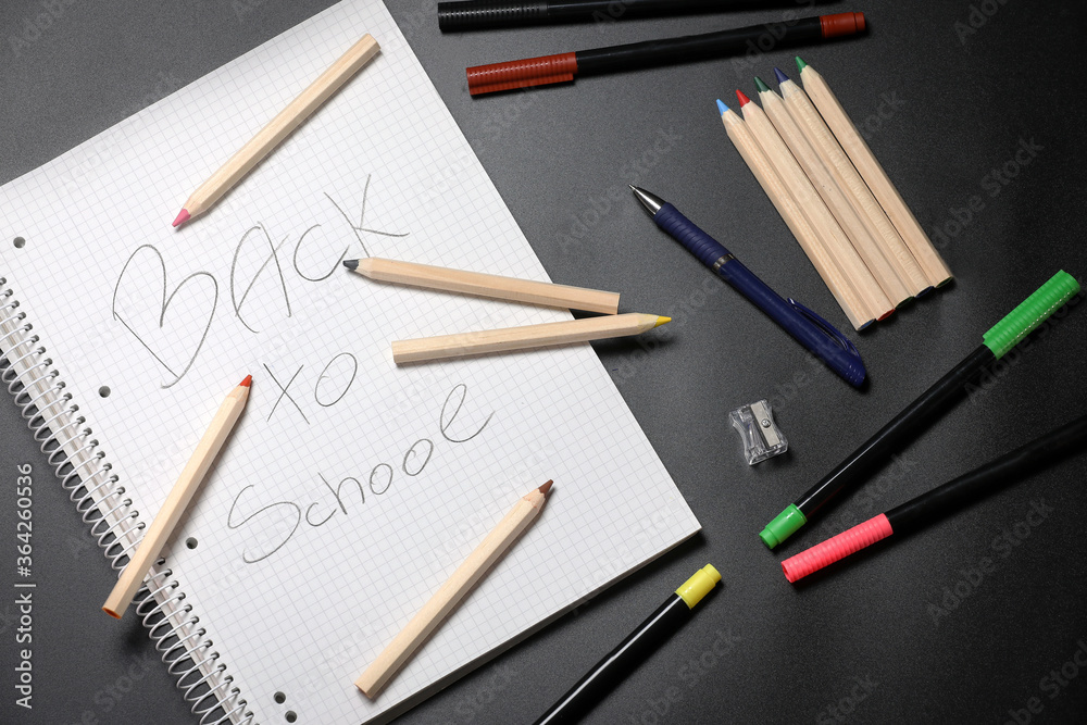 White notebook , color pencils, felt pen and pencil sharpener on a table against black background. Preparing for a school. Back to school. White notebook , color pencils, felt pen and pencil sharpener on a table against black background. Preparing for a school. Back to school.