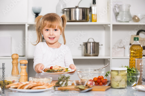 Slika na platnu Playfull girl is demonstraiting plate with salad at home.