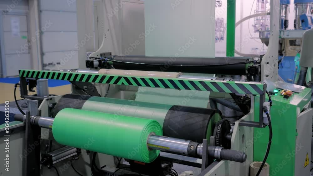 Part of automatic plastic bag making machine - moving roller with flat polyethylene green film at exhibition, trade show. Manufacturing, recycling, industry and automated technology equipment concept Part of automatic plastic bag making machine - moving roller with flat polyethylene green film at exhibition, trade show. Manufacturing, recycling, industry and automated technology equipment concept