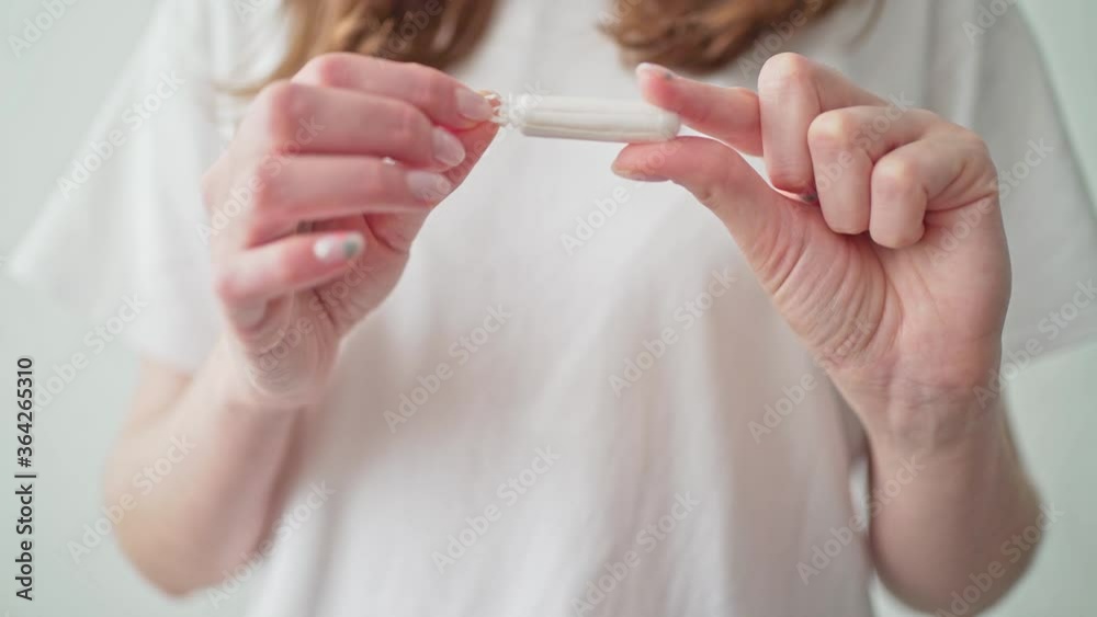 A tampon in women's hands on a white background. Period of menstruation. Protection during menstruation