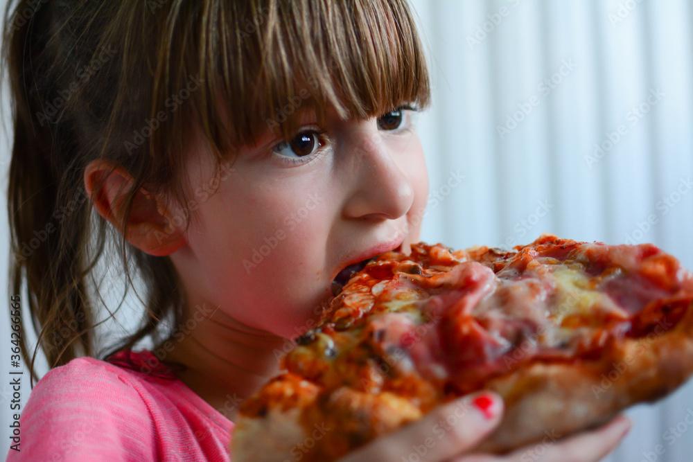 Front view of adorable little girl eating pizza. Happy child eating slice of hot pizza, isolated on white background.