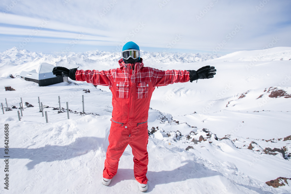 a snowboarder in the mountains with his arms outstretched in a red jumpsuit