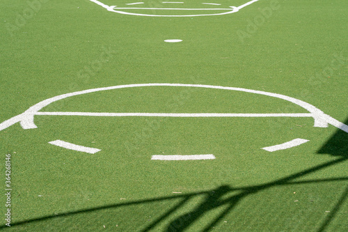 Basket ball court, green grassy ground, artificial grass and white lines. Used by young people in their spare time, to participate in sports activities.
