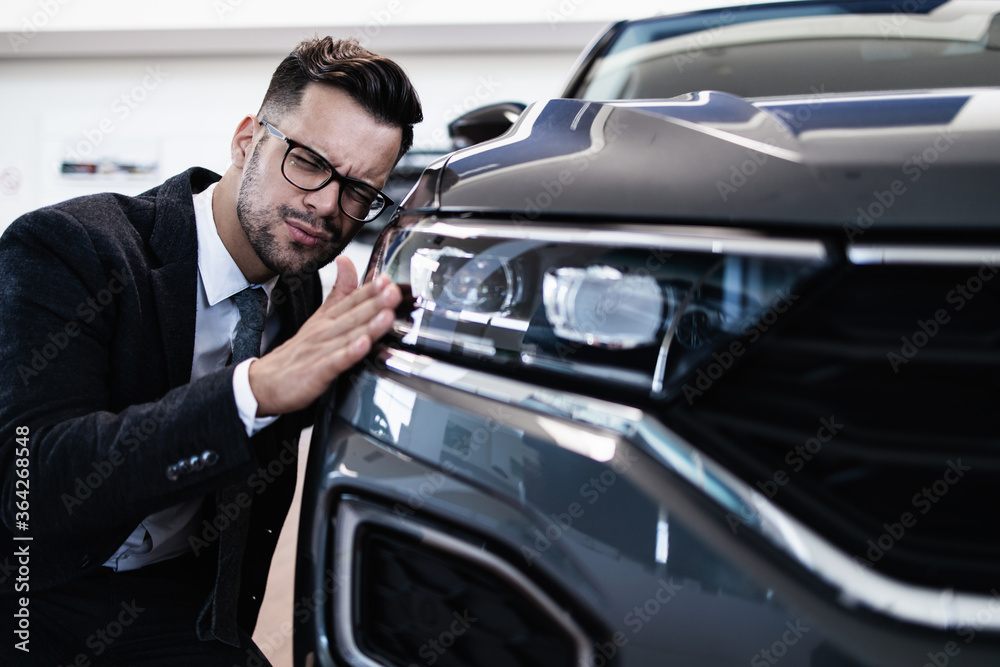 Young handsome businessman choosing and buying his new car in showroom.