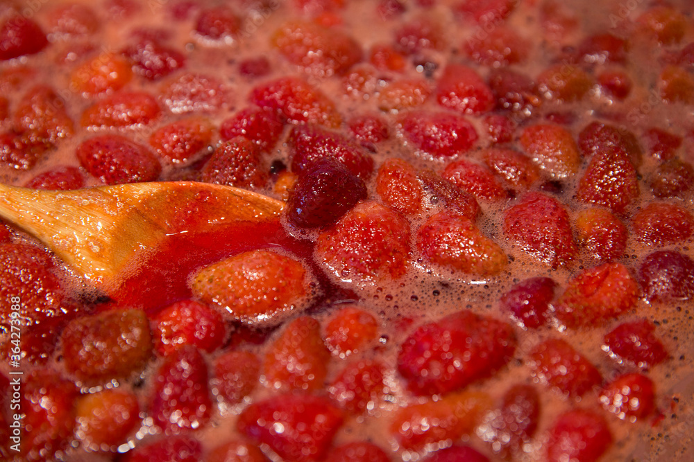 Strawberry Berries in Jam. Cooking strawberry jam. Wooden spoon in a bowl with jam. Blur background. Strawberry Berries in Jam. Cooking strawberry jam. Wooden spoon in a bowl with jam. Blur background.