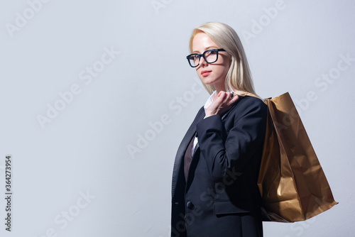 Beautiful blonde businesswoman in suit with shopping bag on gray background