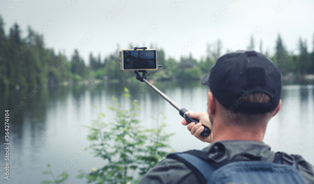 Man holds the smartphone on a selfie stick and records a movie - Holiday memorial film - Traveling in the style of wanderlust - Millennials trekking around the lake Man holds the smartphone on a selfie stick and records a movie - Holiday memorial film - Traveling in the style of wanderlust - Millennials trekking around the lake