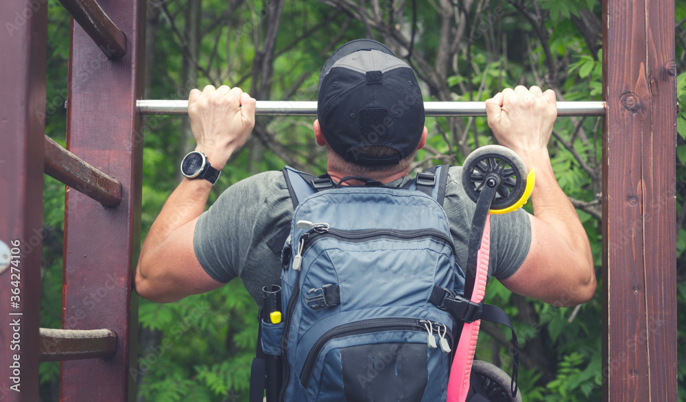 Fototapeta premium Young man pulls himself up - Exercises in the fresh air - Milenials practicing sleep on a ladder - Holiday trip and exercises in the park