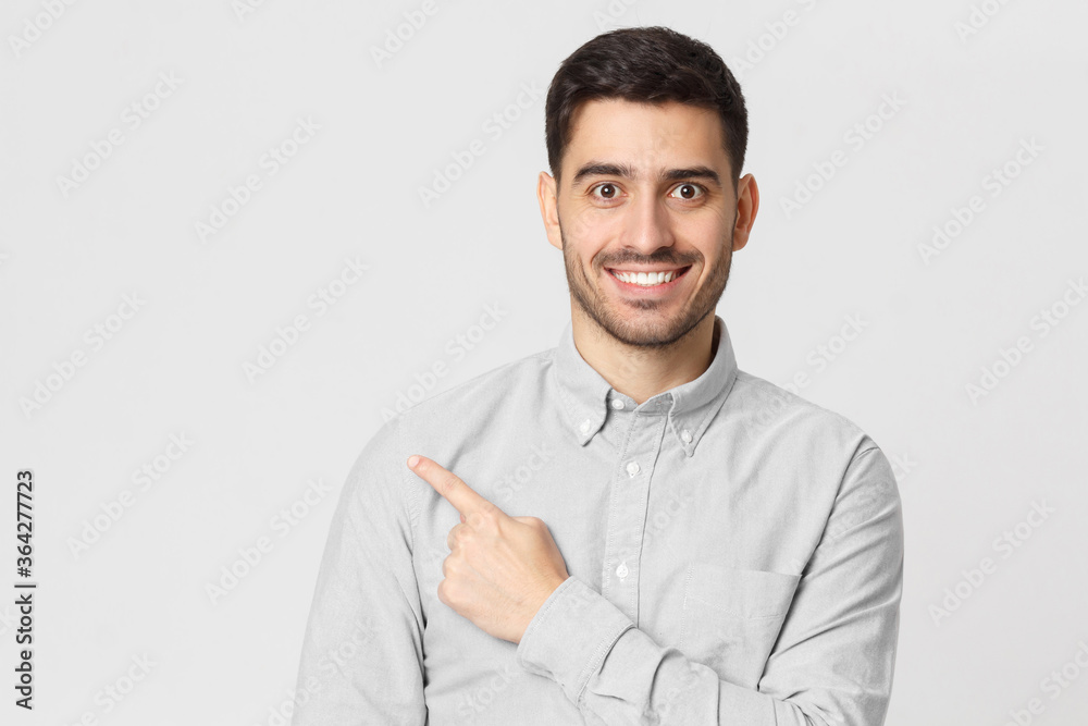 Excited young man in shirt pointing with finger to left side, isolated on gray background Excited young man in shirt pointing with finger to left side, isolated on gray background