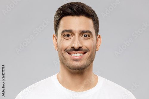 Headshot portrait of young smiling handsome man wearing white t-shirt, isolated on studio gray background