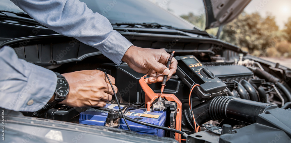 Auto mechanic using measuring equipment tool for fix checking car battery. Concepts of Old car repair service and insurance. Auto mechanic using measuring equipment tool for fix checking car battery. Concepts of Old car repair service and insurance.