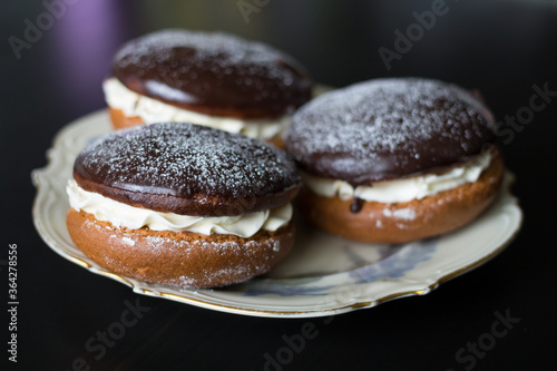 Boucher cakes with cream under chocolate icing on a beautiful white shaped plate on a black background.