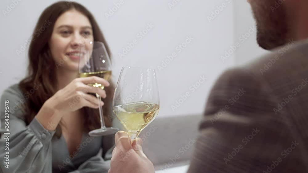 Rear view of young bearded man and his girlfriend sitting in restaurant, clinking glasses with champagne and making a sip Rear view of young bearded man and his girlfriend sitting in restaurant, clinking glasses with champagne and making a sip