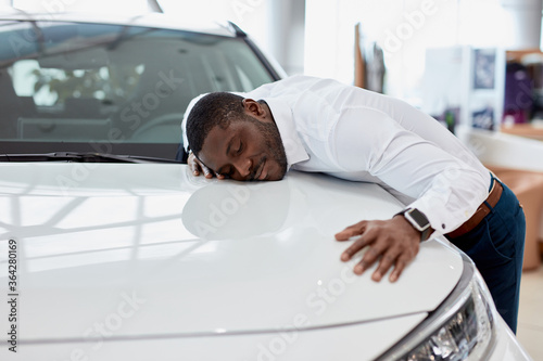 Obraz na płótnie african american man hugs new car he dreams about, he stand in cars showroom nex