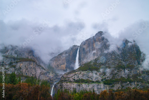 Yosemite National Park in autumn mountains covered in fog with two waterfalls.
