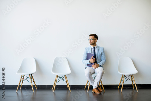 Young man sitting in the waiting room with a folder in hand before an interview photo