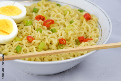 Bowl Of Instant Noodle With leek, Red Chilli and Bamboo Chopsticks On White Background