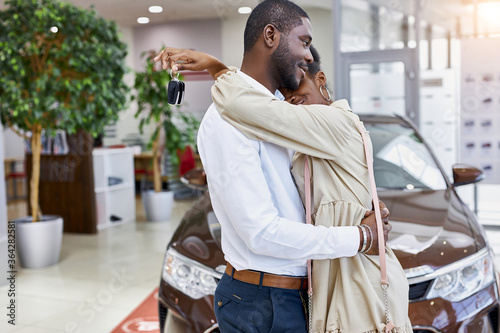 Принти на полотні portrait of cute african married couple hugging each other in car showroom, man
