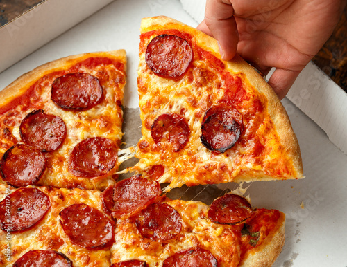 Man taking slice of delicious pepperoni pizza from cardboard box photo