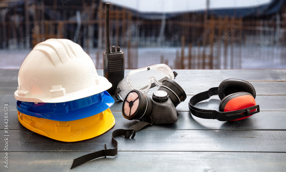 Work safety protection equipment. Industrial protective gear on wooden table, blur construction site background. Work safety protection equipment. Industrial protective gear on wooden table, blur construction site background.