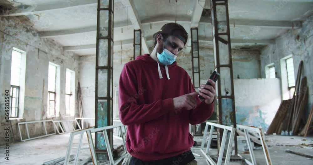 Terrifying evil male zombie walking around the abandoned house. Pale infected undead man in mask scrolling the news feed on the smartphone. Virus, pandemic, infection concept. Terrifying evil male zombie walking around the abandoned house. Pale infected undead man in mask scrolling the news feed on the smartphone. Virus, pandemic, infection concept.