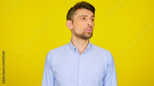 Handsome bearded man looks away on a yellow background with copy space. Guy in a light blue shirt looks in a place for text or goods