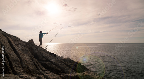 Silhouette of young man fishing on the rocks holding fishing rod with lens flare in phuket Thailand.