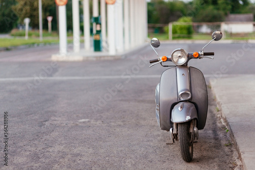 Grey small motorcycle parked on the side of a road at the background of blurred gas station with place for your text photo