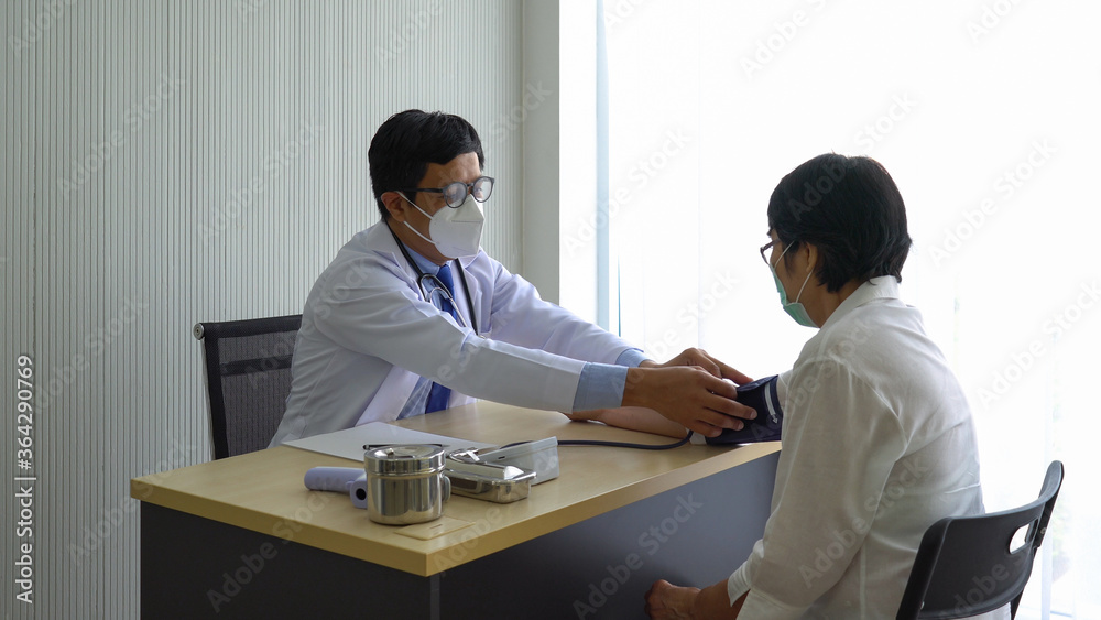 asian doctor using automated digital sphygmomanometer to measure blood pressure of senior woman patient that visit at the hospital because of hypertension. healthcare and medical concept