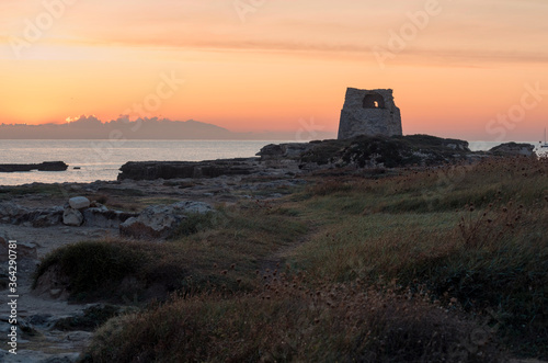 Alba sul mare con torre costiera e cielo arancione.