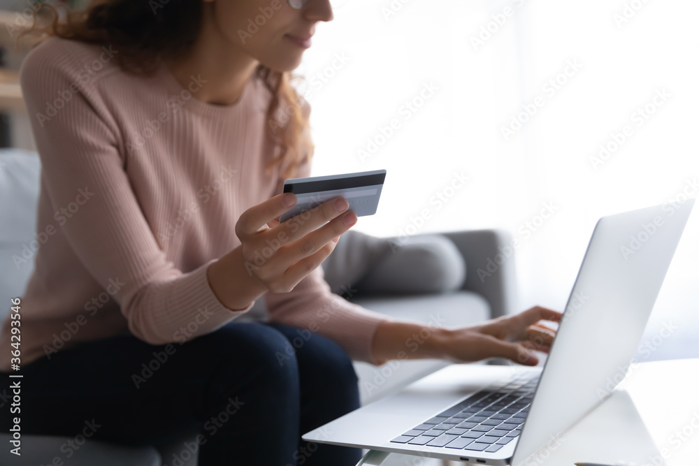 Crop close up of millennial female sit on couch at home make online payment on internet banking system on computer, young woman buying shopping on web, use credit card for purchase