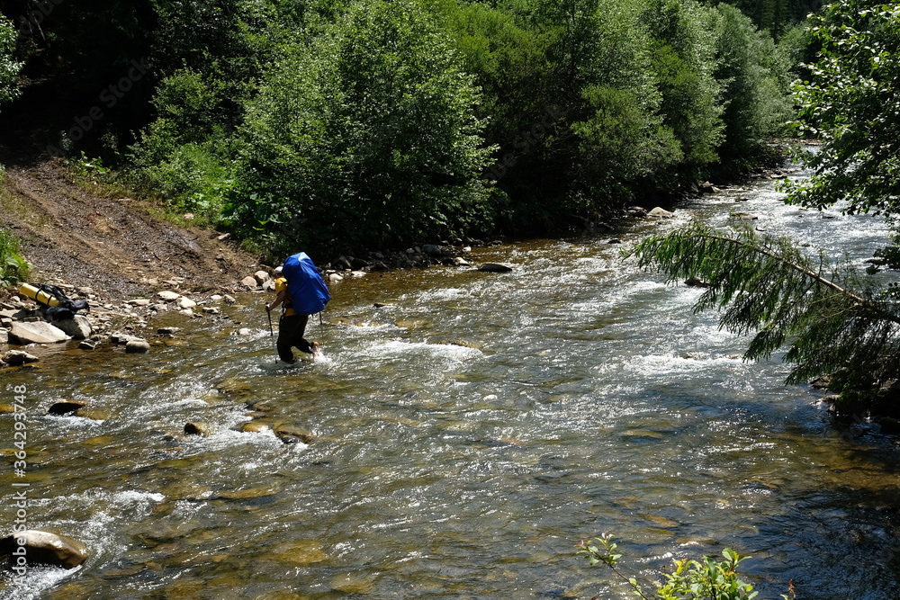 Hiker man crossing a river using trekking poles