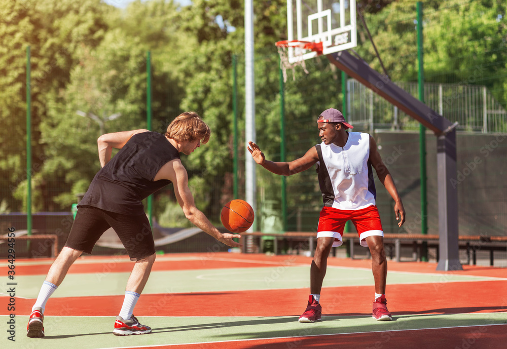 African American and Caucasian basketballers playing game match at outdoor court
