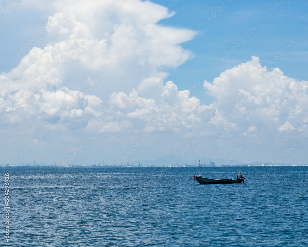 A man sits on a boat and fishing in the sea under blue sky with cloud.