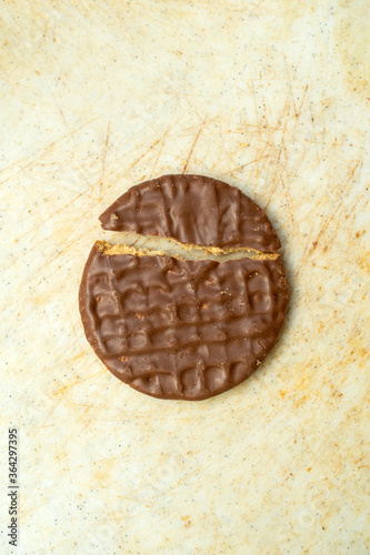 Delicious hocolate covered cookie or biscuit broken in two on plastic chopping block.