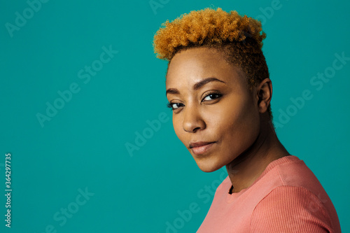 Portrait of a serious young african female with cool short hair looking at camera, against studio background
