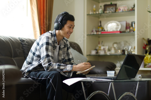 Happy teenage of asian people writing a note and looking at laptop computer while stuying or working at home. photo