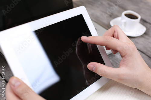 Hands holding tablet on wood table with tea