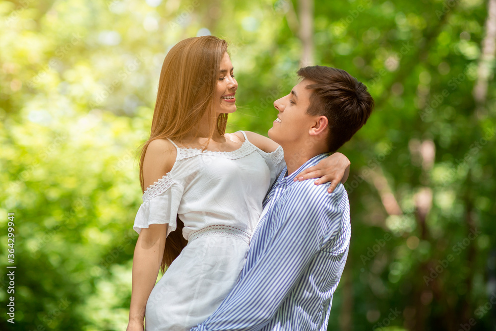 Tender young man holding lovely girlfriend in his arms outdoors on sunny day Tender young man holding lovely girlfriend in his arms outdoors on sunny day