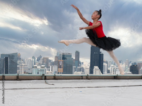 Ballet girl students show jumping skills while performing outdoors on a high-rise building.