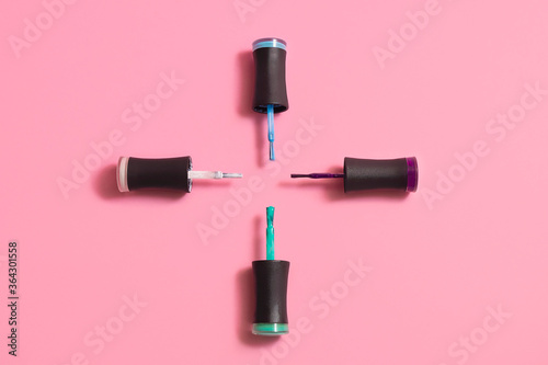 Top view of different color nail polish bottles on pastel pink background