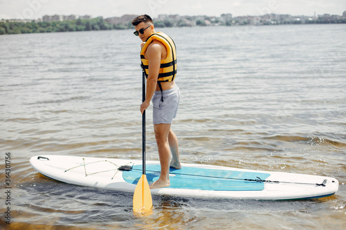 Canvas Print Handsome man with a sup. Surfer in a yellow vest.
