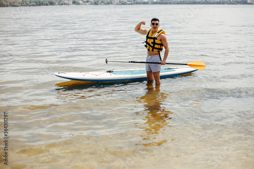 Handsome man with a sup. Surfer in a yellow vest. © prostooleh
