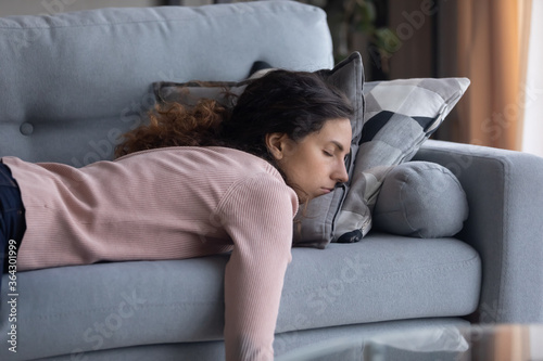 Tela Exhausted young Caucasian woman lying on comfortable sofa in living room sleepin